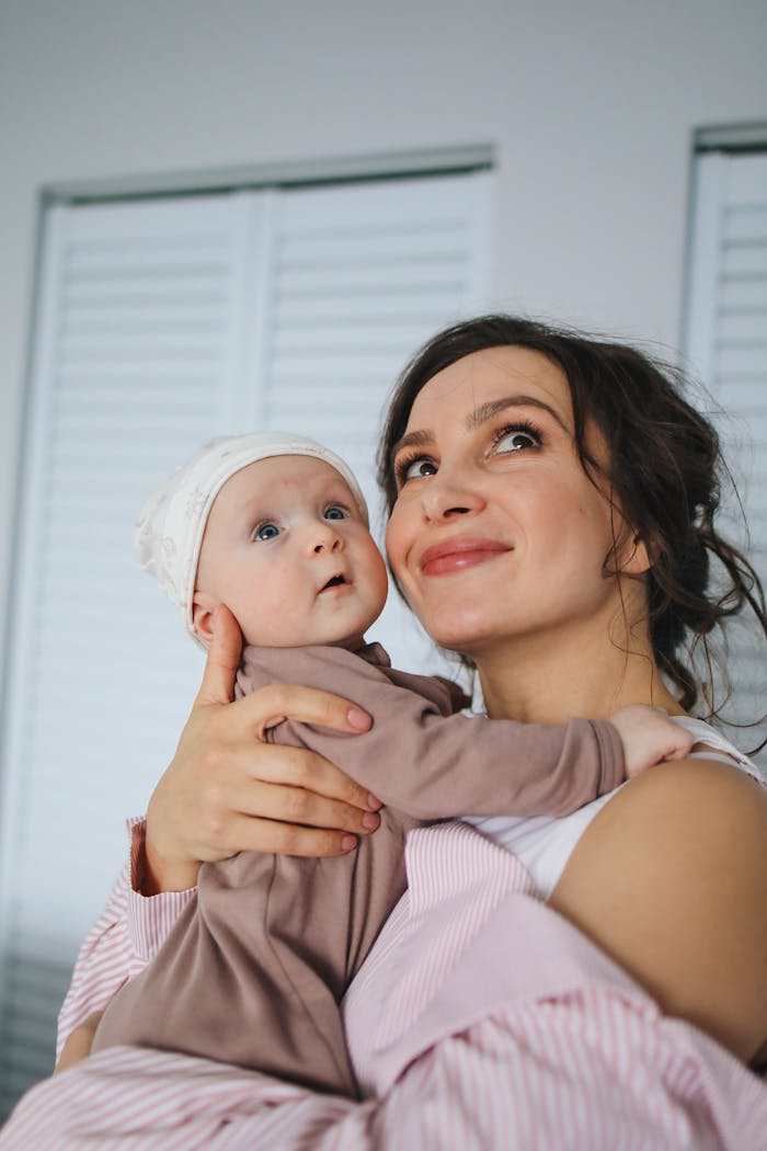 Woman in White and Pink Striped Long Sleeve Shirt Carrying Baby Wearing Brown Onesie